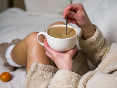 Bornozlu kadın beyaz yatakta oturur, kaşık kaşık ile kahve karıştırır, mandalinalarla çevrili, rahat sabahında kahveden zevk alır. Canlı mandalinalar kahve anlarına sıcaklık katar. 