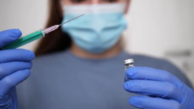Cerrahi maske takan, eldiven takan, şırınga ve şişeyle aşı hazırlayan, önemli aşı işlemleri sırasında aşı yaparken güvenlik ve bakımı sağlayan kadın tıp uzmanı.. 