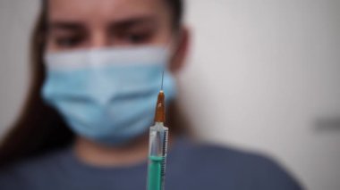 Tıbbi uzman koruyucu giysi giyip aşıyı hazırlarken şırıngayı steril hastane ortamında şırıngayla hazırlıyor. Aşıyla ilgilenirken hassasiyet ve bakıma odaklanıyor. 