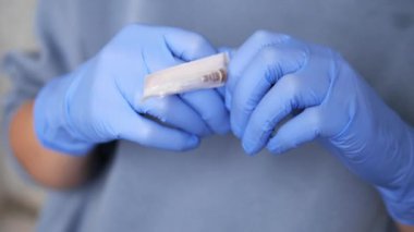 Mavi eldiven giyen tıp uzmanı şırınga iğnesi, hijyen ve güvenlik içeren steril paketi dikkatlice açarken şırınga ve tıbbi aletlerin tam olarak nasıl kullanılacağı üzerine odaklanıyor.. 