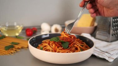 Balanesi makarna tabağı hazırlanıyor, bir şef çatalla spagetti çeviriyor, tabağın üzerine porsiyon kaldırıyor, domates, sarımsak, fesleğen, zeytinyağı ve peynir rendesi gibi malzemelerle çevrili.