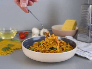 Şef, mutfaktaki domates, mantar, zeytinyağı, fesleğen, fesleğen ve çiğ spagetti gibi malzemelerle makarnayı kaseden çatalla kaldırıyor.