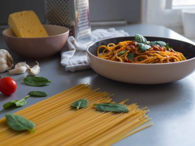 Üzerinde domates sosu ve fesleğen yaprakları olan peynirli, sarımsaklı, vişneli, domatesli ve ıspanaklı taze malzemelerle çevrili gri bir masada.