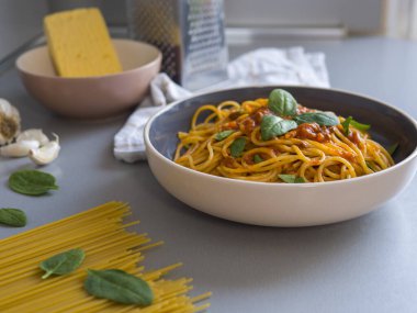 Domates soslu ve fesleğenli Balanesi makarna, gri bir masada servis edilen çiğ makarna, sarımsak karanfili, parmesan peyniri ve arka planda rende