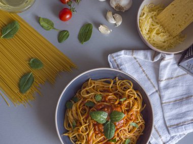 Domates soslu ve taze fesleğenli Balanesi makarna, çiğ spagetti, kiraz domatesleri, sarımsak ve rendelenmiş peynir ile çevrili, canlı bir mutfak sahnesi yaratır.