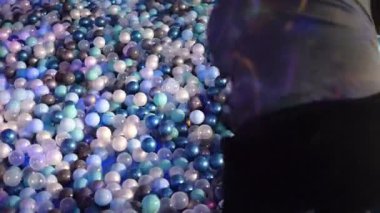 Oyuncu baba, küçük oğlunu top havuzunda döndürür ve o anı neşeyle doldurur. Baba, açık mavi, koyu mavi, beyaz plastik toplarla çevrili çocuğu döndürür. Baba, oğlunu döndürür ve eğlenceli dinamik bir sahne yaratır. 