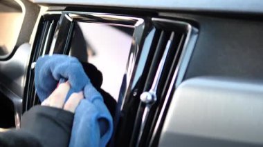 Profesyonel kadın, mavi mikrofiber bezle arabanın ön camını dikkatlice temizliyor. Araba havalandırması ve tablet ekranı tertemiz olur. Arabanın içini temizlemek görüş ve parlaklığı arttırır.. 