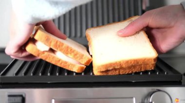 Profesyonel şef, jambonlu sandviçleri elektrikli tost makinesine dikkatlice yerleştirir ve mükemmel bir kıtır kıtır olmasını sağlar. Elektrikli tost makinesi malzemeleri eşit ısıtır, lezzeti artırır 