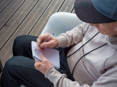 Yaşlı adam ahşap verandada sessizce oturur, kişisel not defterine düşünceli notlar yazar. Yaşlı adam huzurlu bahçe manzarasının tadını çıkarıyor. Yaşlı adam sakin bir açık hava anını kucaklıyor.. 