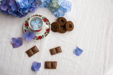 Üzerinde çiçekler ve çikolatalı bisküviler olan bir fincan.