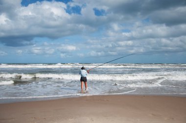 Yaşlı kadın sahilde balık tutuyor.