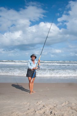 Yaşlı kadın sahilde balık tutuyor.