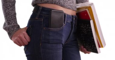 Beyaz arka planda cebinde telefonla kitap taşıyan üniversiteli bir kızın yakın çekimi. Elinde kitap, cebinde cep telefonu olan bir kadının orta bölümünün yakın çekimi. 4k