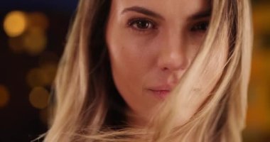 Şehir ortamında saçları rüzgarda dalgalanan güzel genç bir bayana yakın durun. Kahverengi gözlü ateşli kadın kameraya bakıyor. 4k