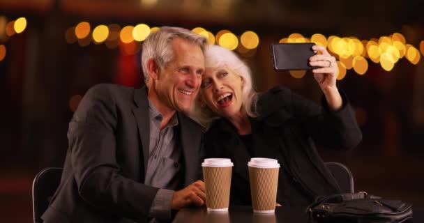 スマートフォンでセルフィーを撮る夜のデートでシニアカップル 幸せな高齢者のカップルのスマートフォンで写真を撮る — ストック動画