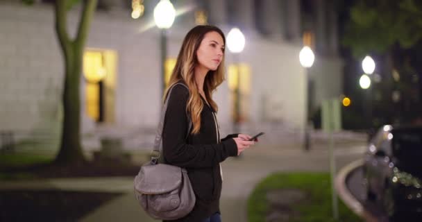 20多岁的白人女性用手机发短信 晚上站在校园图书馆外面 白人千年或学生在晚上用智能手机在大楼外发短信 — 图库视频影像