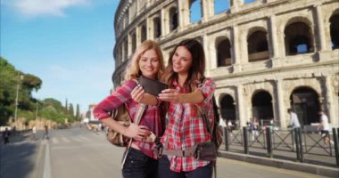 Roma, İtalya 'da, Colosseum' un önünde selfie çekerken mutlu sarışın ve esmer. Seyahat eden en iyi bayan arkadaşlar Roma 'da telefon kamerasıyla fotoğraf çektiriyorlar. 4k