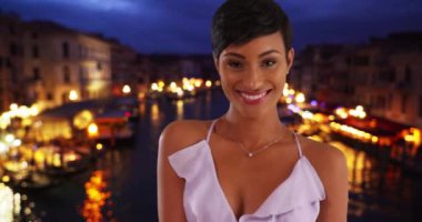 Venedik, İtalya 'daki güzel Afrikalı Amerikalı kadın turist Grand Canal' da yaz gecesinin tadını çıkarıyor. Güzel bir yaz elbisesi içinde poz veren neşeli, gülümseyen siyah kadın portresi. 4k