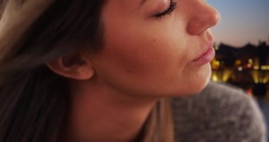 Dışarıdaki nazik genç bayanın saçlarını tek başına düşünen rüzgarın aşırı yakın çekimi. 20 'li yaşlarda, gözleri kapalı, akşamları dışarıda huzurlu görünen bir kız. 4k