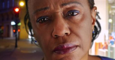 Yaşlı siyahi kadın gecenin bir yarısı şehir sokağında dikilip hüzünlü bir şekilde uzaklığa bakıyor. Gözlerinde yaşlarla Afrikalı Amerikalı bir kadının portresi. 4k