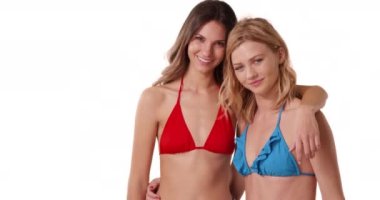 Beyaz fotokopi alanında poz veren bikinili iki mutlu beyaz kadının portresi. Neşeli esmer ve sarışın beyaz arka planda birbirlerini kucaklıyorlar. 4k