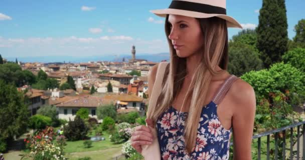 イタリアのフィレンツェで休暇中にフェドーラを着て袋を持っている花の部屋のきれいな女性 フィレンツェ旅行中の夏服を着た20代のスタイリッシュな若い女性 — ストック動画