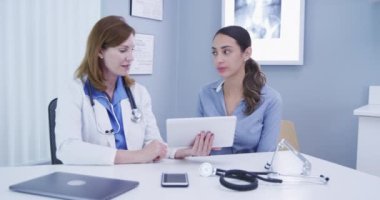 Sağlık durumunun sonuçlarını paylaşmak için tablet bilgisayar kullanan kıdemli tıp doktoru. Orta yaşlı doktor ve genç hasta kapalı bir klinikteki yüksek teknoloji tabletine bakıyor.