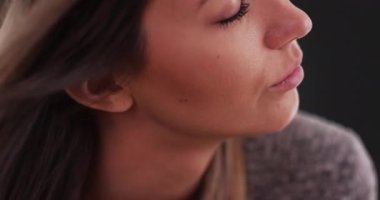 Rüzgarın aşırı yakın planında gri zeminde genç bayanın saçları uçuşuyor. 20 'li yaşlarda, gözleri kapalı gri arka planda huzurlu görünen bir kız. 4k