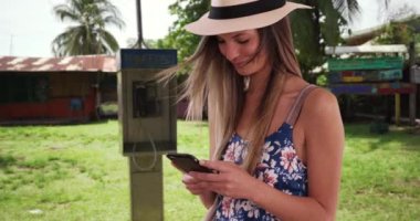 Çiçekli Romper ve fötr şapkalı mutlu bir kadın tropik bir kasabada telefonla mesajlaşıyor. 20 'li yaşlarda Kosta Rika' dayken cep telefonundan mesaj atan bir kız. 4k