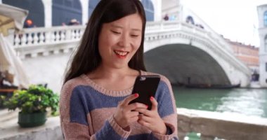 Akıllı telefon kullanan ve İtalya Venedik 'teki Rialto köprüsünün önünde kısa mesajlar okuyan genç turist. Sevgili Asyalı kadın milenyum kuşağının Avrupa 'dan cep telefonuyla gönderdiği mesajları kapatın. 4k