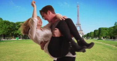 Beyaz bir adam sevgilisini Eyfel Kulesi 'ne doğru taşıyor. Paris 'teki parkta oynayan turist çift, gülümsüyor ve gülüyor. 4k