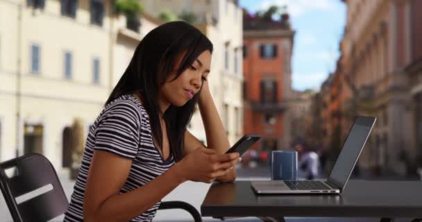 携帯電話をチェックするために休憩を取って彼女のラップトップで働いている黒人女性 ローマのビジネス女性や学生の側のビューは 都市部の通りに彼女のコンピュータ上で動作します — ストック動画