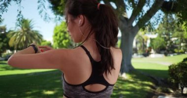 Atletik milenyum kadını şehir ortamında akıllı saati kontrol ediyor. Açık havada kalp atışlarını izlemek için kol saatine bakan sportif bayan koşucu. 4k