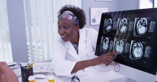 非洲资深医生的特写镜头 向年轻病人解释他的颅骨扫描 聪明的女医生用电脑扫描病人的大脑 — 图库视频影像