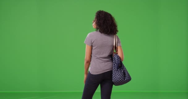 黑色女人的后视镜 蓝色的大圆点袋耐心地等待在绿色的屏幕上 身着休闲装的女孩身后的中镜头 站在绿屏上环视四周 寻找键音或作曲 — 图库视频影像
