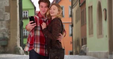 Milenyum çifti Avrupa 'da tatilde cep telefonuyla selfie çekiyor. Çekici erkek ve kadın turistler aptalca suratlar yapıp akıllı telefonlarda fotoğraf çekiyorlar, gülümsüyor ve gülüyorlar. 4k