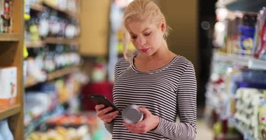 Marketteki kadın ton balığı konservesinin üzerindeki beslenme bilgilerini kontrol ediyor. Annemin süpermarketten aldığı telefonla çekilmiş bir portresi. 4k