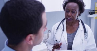 Hasta sağlık bilgilerini görmek için elektronik not defteri tableti kullanan siyah doktoru yakından görmek. Afrikalı kadın doktorun genç bir hastaya sağlık sorununu açıklarken çekilmiş bir fotoğrafı.