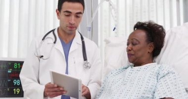 Hastane yatağında tablete bakarak iyileşen pozitif siyah kadın hasta. Hasta ameliyat sonuçlarını paylaşmak için elektronik not defteri tableti kullanan yakışıklı Latin doktor.