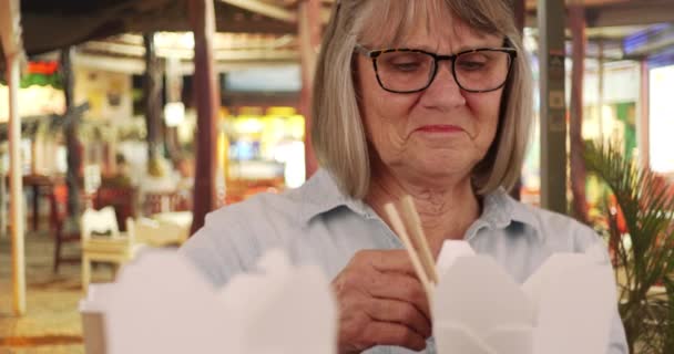 幸せな高齢者の女性が自信を持って屋外のテーブルに座って彼女のフォーチュンクッキーを披露 外で中華料理を食べた後の幸せ先輩女性読書福の肖像画 — ストック動画