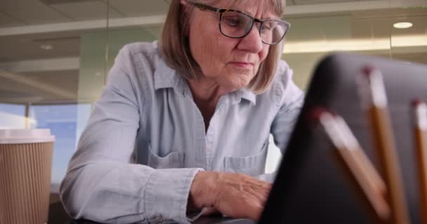 高级妇女在公司工作场所的笔记本电脑上打字的特写镜头 在现代办公空间设置中使用手提电脑的老年妇女的画像 — 图库视频影像