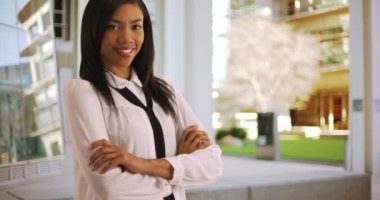 Ofis binasının dışında kolları bağlı poz veren neşeli bir iş kadını portresi. Başarılı Afrikalı Amerikalı kadın kameraya gururla gülümsüyor. 4k