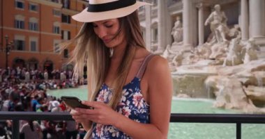 Roma, İtalya 'yı keşfederken çiçekçi tulumu ve fötr şapkalı mutlu bir kadın telefonla mesaj atıyor. 20 'li yaşlarda bir kız Trevi Fountain' ın cep telefonundan mesaj atıyor. 4k
