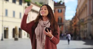 Telefonuyla arkadaşına el sallayan gülümseyen Latin kadın. Gülümseyen ve selam veren çekici bir kadının portresi. 4k