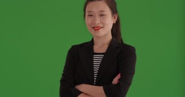 Çekici Asyalı genç iş kadını kameraya gülümsüyor ve yeşil ekranda kollarını kavuşturuyor. Yeşil ekranın önünde neşeli görünen oldukça profesyonel bir kadın. 4k