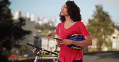 Çekici siyahi kadın San Francisco 'da yol tarifi için cep telefonunu kullanarak bisiklet sürerken kaybolmuş. Yerleşim bölgesinde elinde bisiklet kaskı olan Afrikalı bir kadın sokak tabelasına bakıyor. 4k