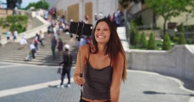 Güzel bir milenyum kızı Roma 'da tatilde İspanyol Merdivenleri' nde selfie çekiyor. İtalya 'daki genç turist kadın selfie çubuğu kullanıyor, gülümsüyor ve surat yapıyor. 4k