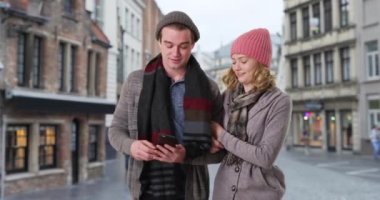 Çekici beyaz erkek ve kadın Belçika sokaklarını kol kola geziyor. Turistler yön bulmak için akıllı telefon kullanıyor. 4k