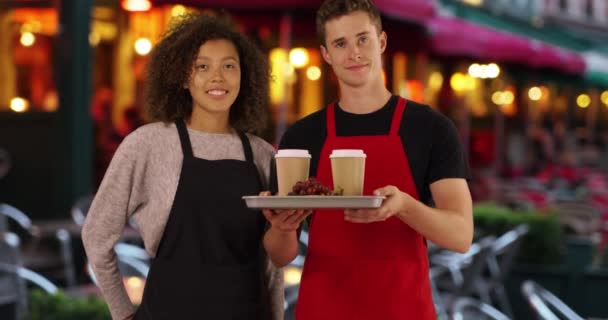 フレンドリーな男性と女性のウェイターは肖像画のポーズ カフェの外でコーヒーのトレイを保持する2つの多民族バリスタ — ストック動画