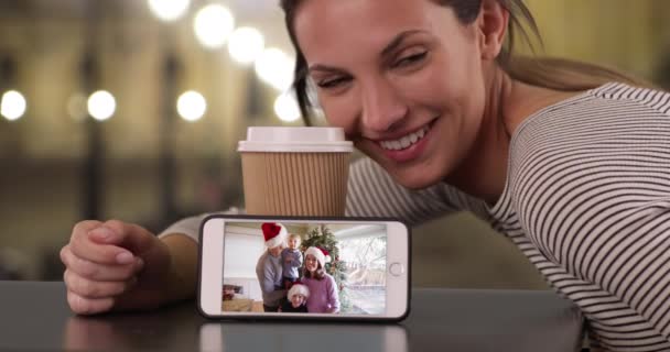 クリスマスの間に親戚の電話ビデオを示すコーヒーと一緒に座っている幸せな女の子 幸せな家族の休日を祝う電話でビデオクリップを示す笑顔ブルネットの女性 — ストック動画